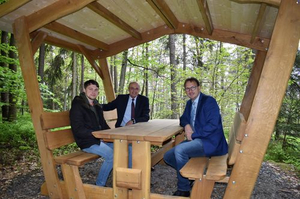 Geschäftsführer des Naturparks Haßberge Lukas Bandorf, Landrat Wilhelm Schneider und Bürgermeister Wolfram Thein sitzen in der neuen Sitzgruppe